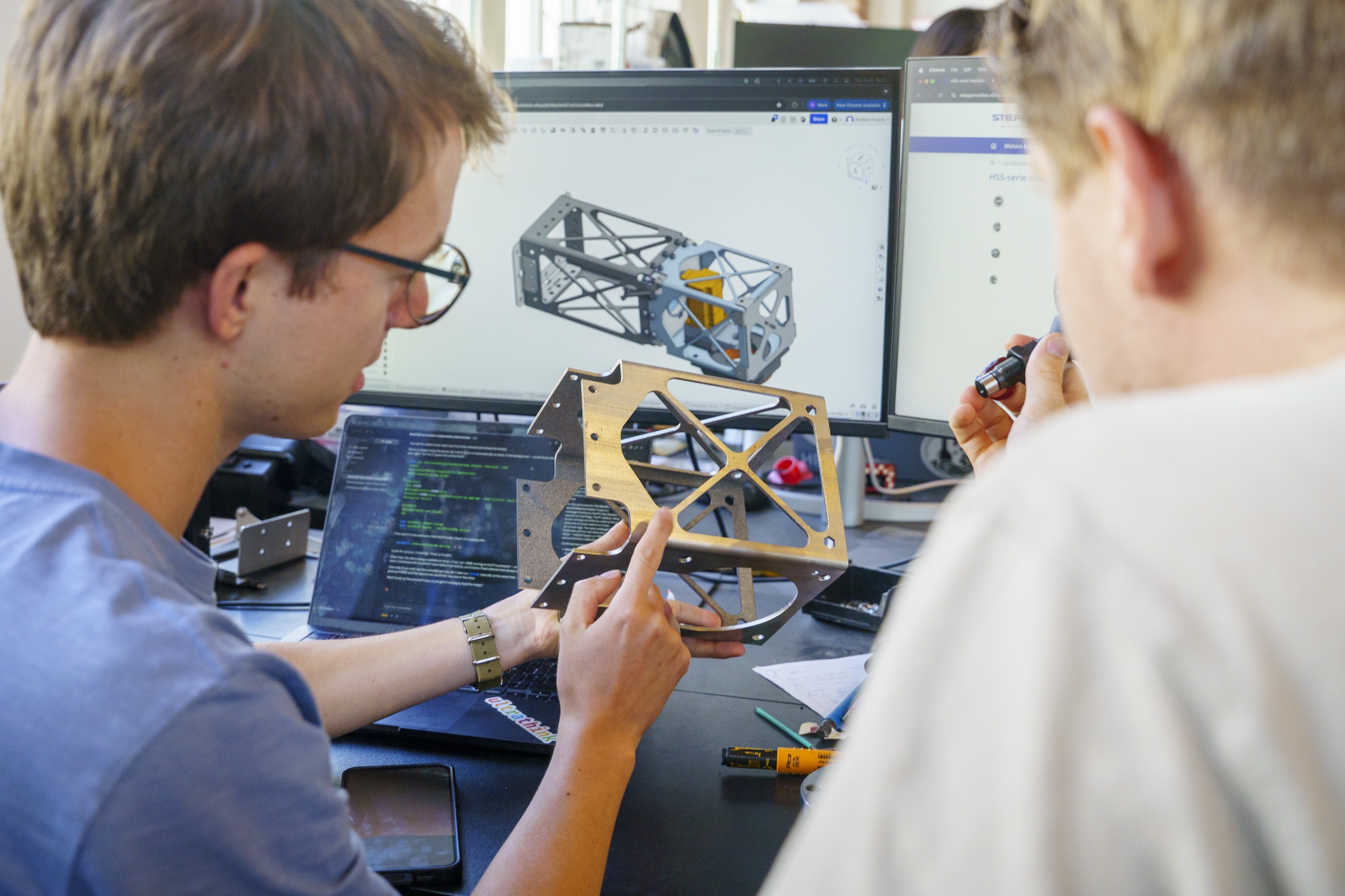 Two Monumental engineers reviewing a machined robot part alongside its CAD model in the Amsterdam office