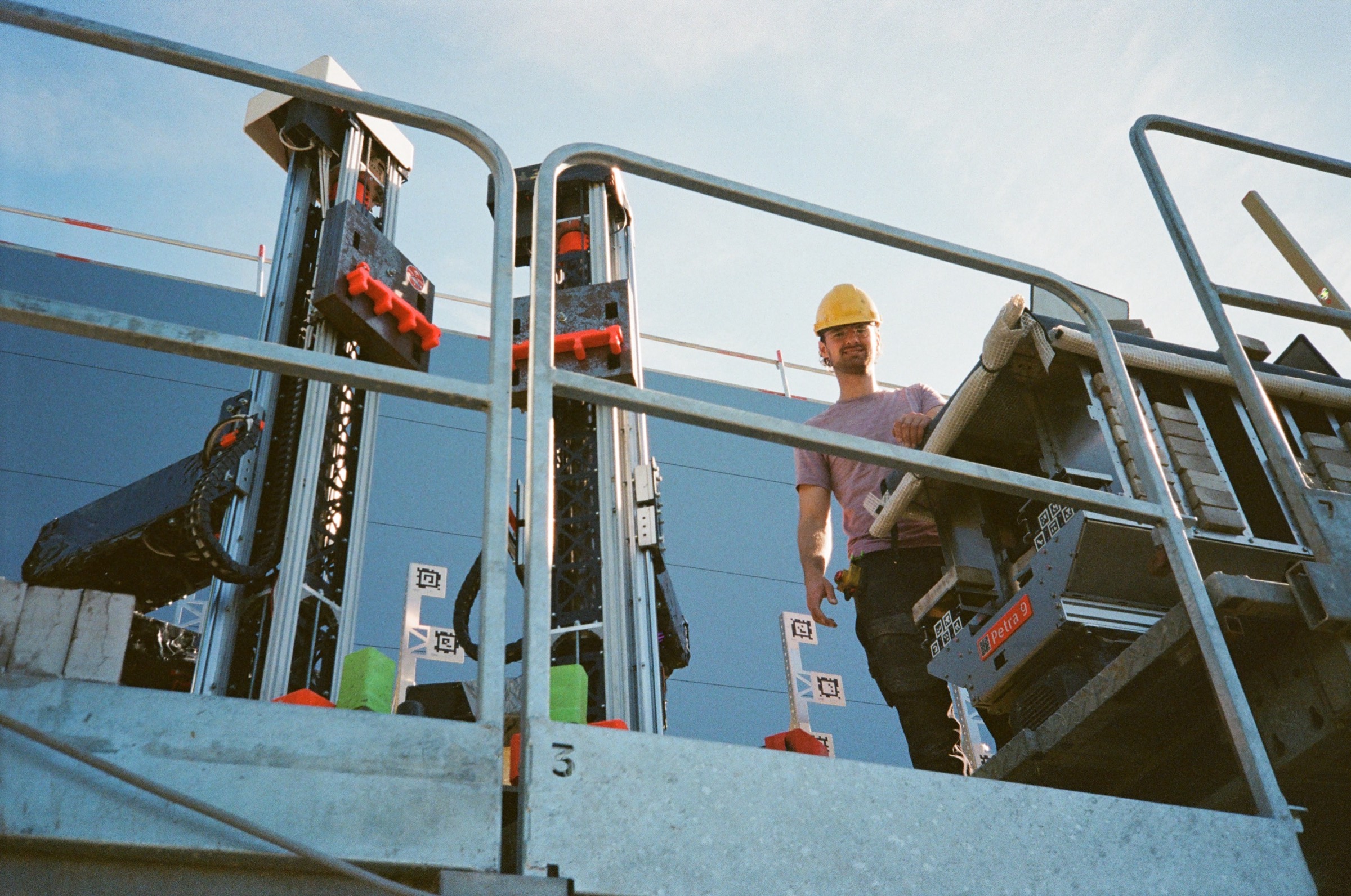 A Monumental engineer on the platform of a bricklaying robot against a clear blue sky